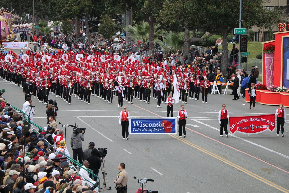 The Red Raider Marching Band of Pulaski, Wisconsin, in red and white, marches a parade route past spectators.
