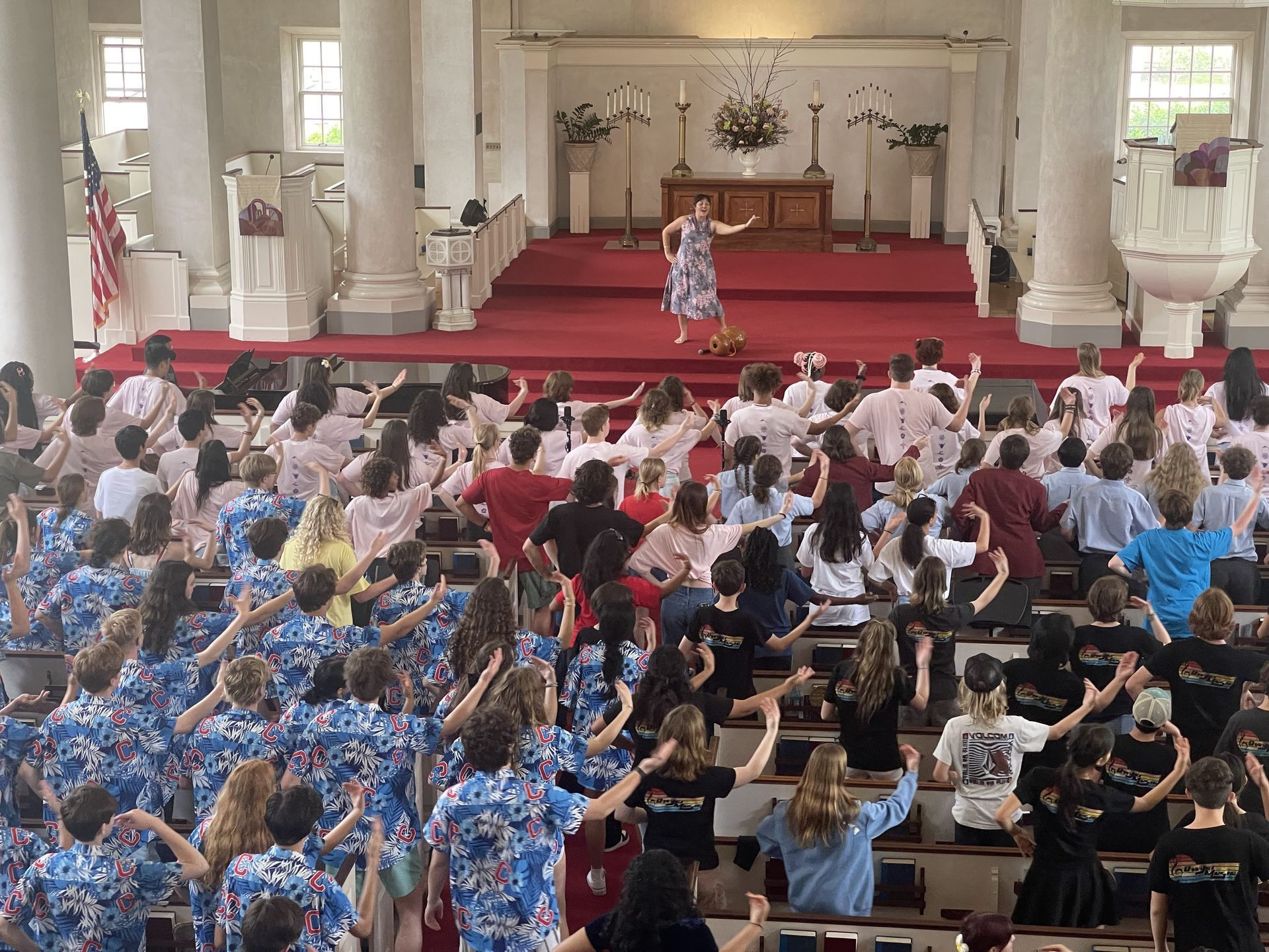 Singers raise their hands toward a leader on a red-carpeted platform at the Aloha State Choral Festival.